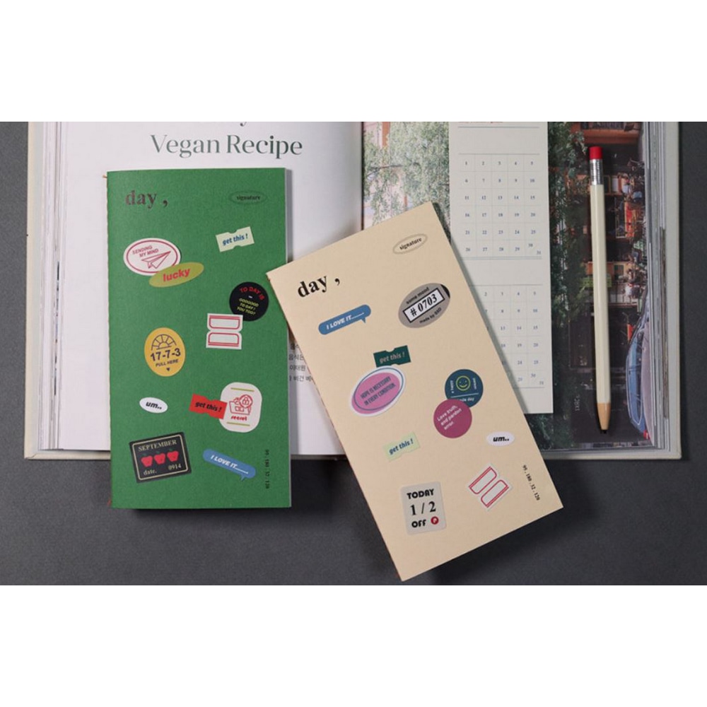 Signature Planner Daily Leafgreen und Ivory mit Mingle Stickern beklebt auf einem Kochbuch mit dem Text Vegan Recipe. 
